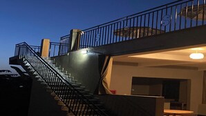 A staircase leading to an upper level with a railing, a table, and a bench on the ground floor. - Stevalyn's Ridge View Lodge (Jinja)