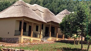 A building with a unique thatched roof, a stone foundation, and a balcony with a railing. - Stevalyn's Ridge View Lodge (Jinja)