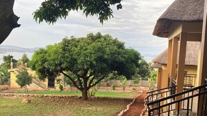 A tree-lined pathway leading to a building with a thatched roof. - Stevalyn's Ridge View Lodge (Jinja)