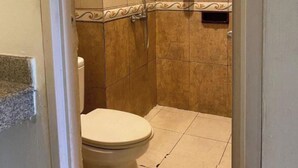 Un baño pequeño con baldosas, que incluye un inodoro, una ducha y dispensador de jabón en la pared.