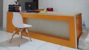 Una recepción con una silla blanca, una cafetera y un monitor de computadora.