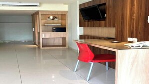 Una habitación moderna con un escritorio de madera, una silla roja, un televisor de pantalla plana montado en la pared y una estantería empotrada.