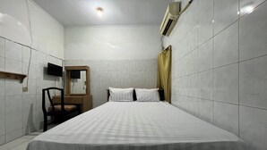A small, clean room with white tiled walls, a bed with white bedding, a wooden nightstand, a chair, a mirror, and an air conditioning unit. - Hotel O Kost Stan (Negeri Lama)