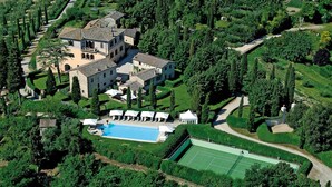 An aerial view of a large estate with a swimming pool, tennis court, and multiple buildings surrounded by lush greenery. - Villa Camelia by Elite Villas (Colle di Val d'Elsa)