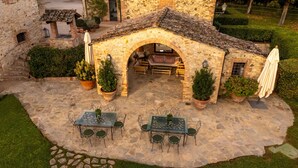 An outdoor patio with stone flooring, two tables with chairs, and potted plants. - Villa Camelia by Elite Villas (Colle di Val d'Elsa)