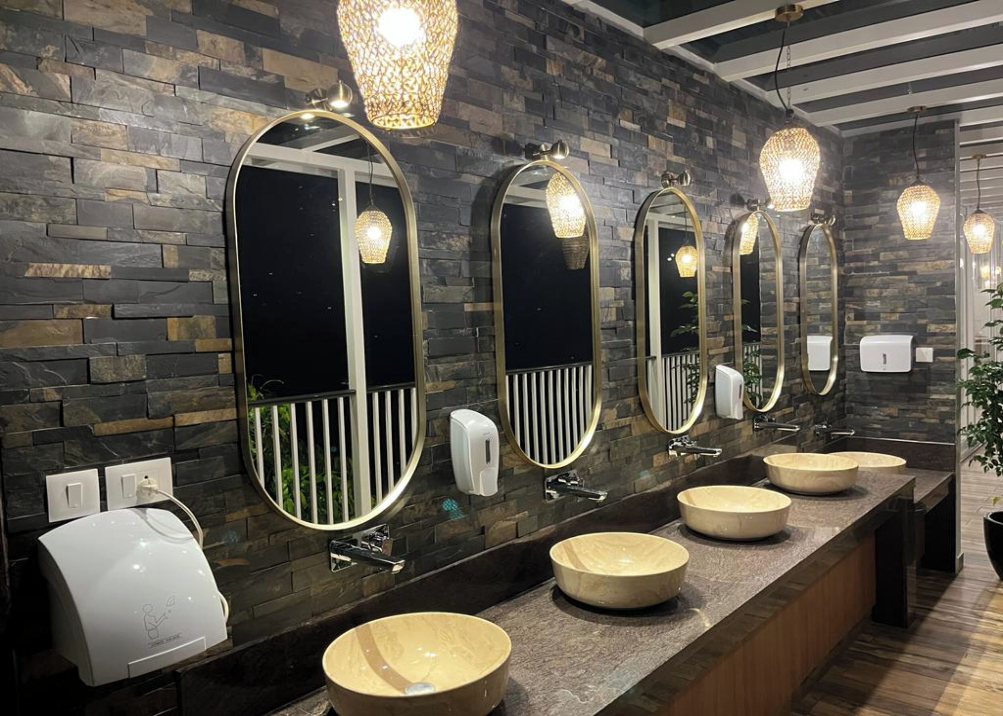 Ein modernes Badezimmer mit Steinwänden, mehreren Waschbecken und großen Spiegeln.