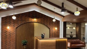 A reception area with a wooden reception desk, a potted plant, and a leather couch. - British County Resort (Devikolam)