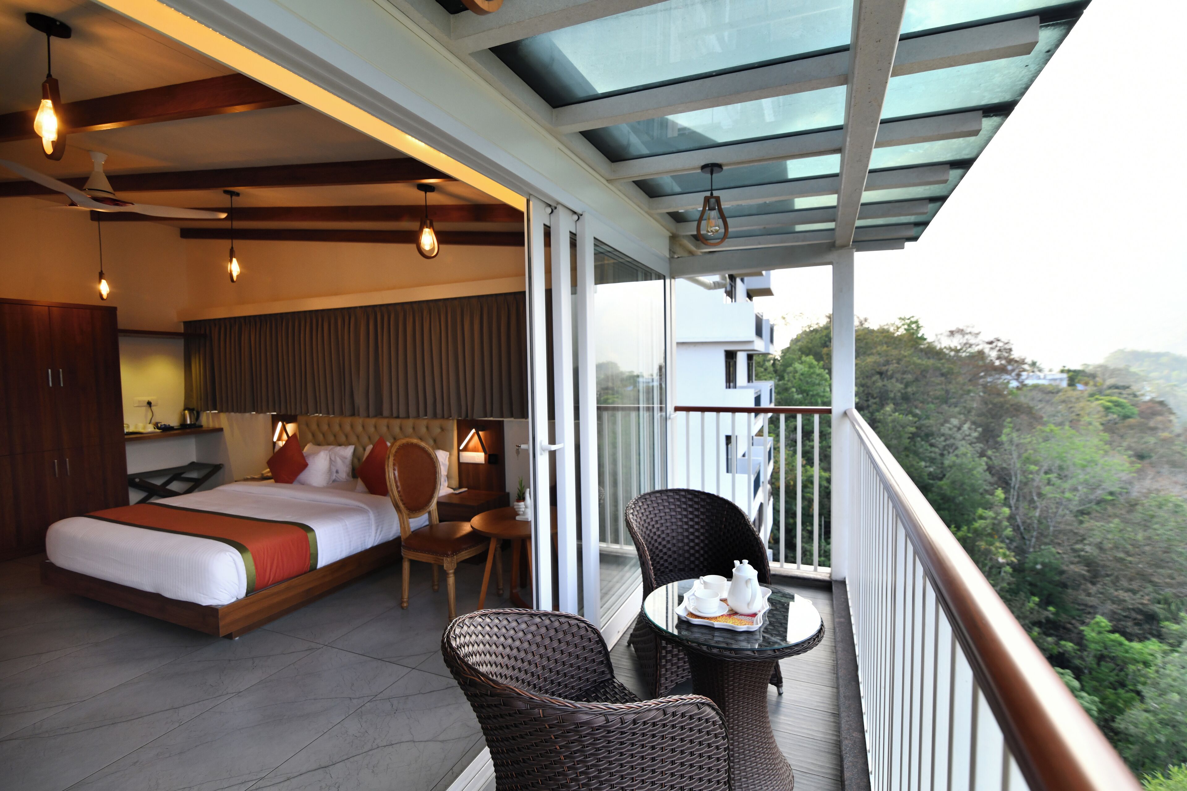 Une chambre d’hôtel comprenant un lit, une table à manger avec des chaises et un balcon offrant une vue sur la forêt.