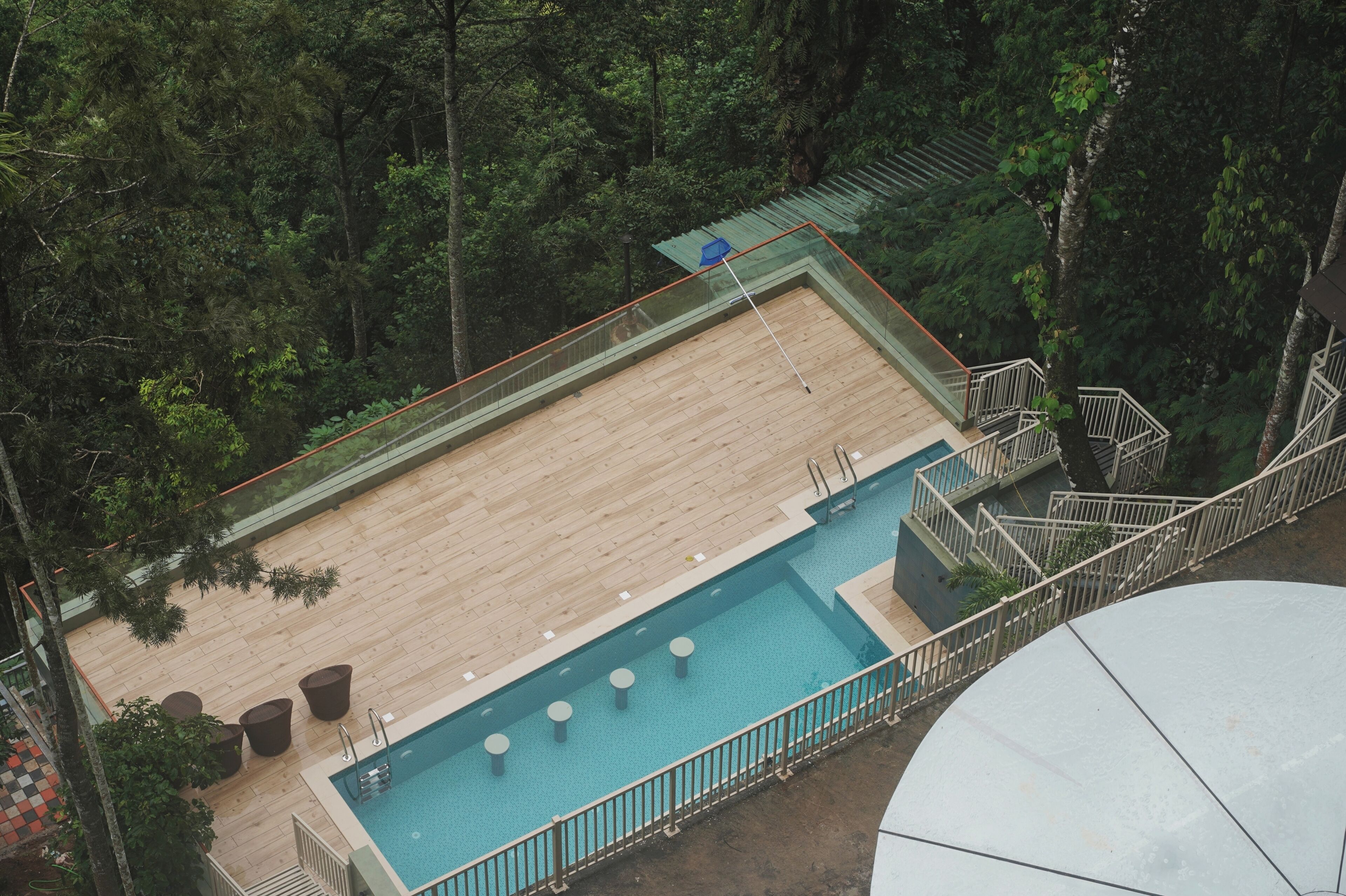 Ein Pool auf dem Dach mit einer Holzterrasse, umgeben von Bäumen und einem Glasgeländer.