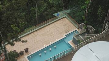 Ein Pool auf dem Dach mit einer Holzterrasse, umgeben von Bäumen und einem Glasgeländer.