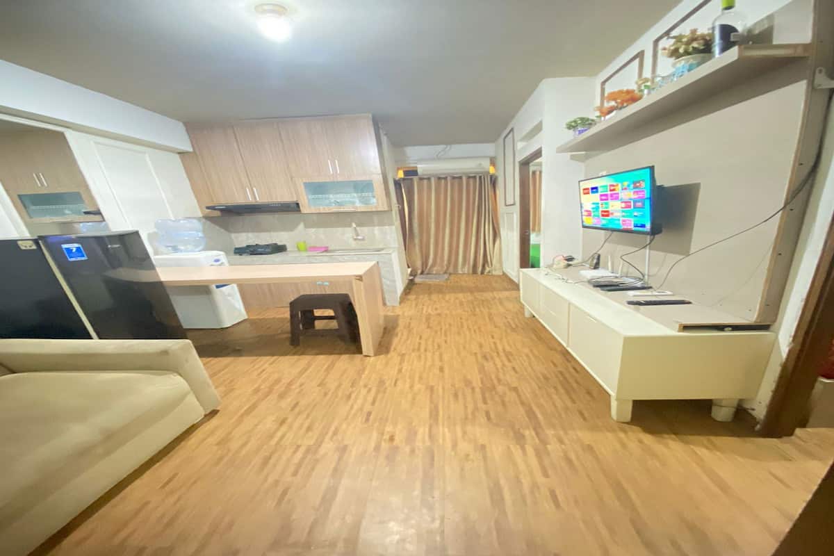 Une cuisine compacte avec des meubles blancs, un réfrigérateur, un four à micro-ondes et un petit plan de travail. Le sol est en bois et un téléviseur est fixé au mur.