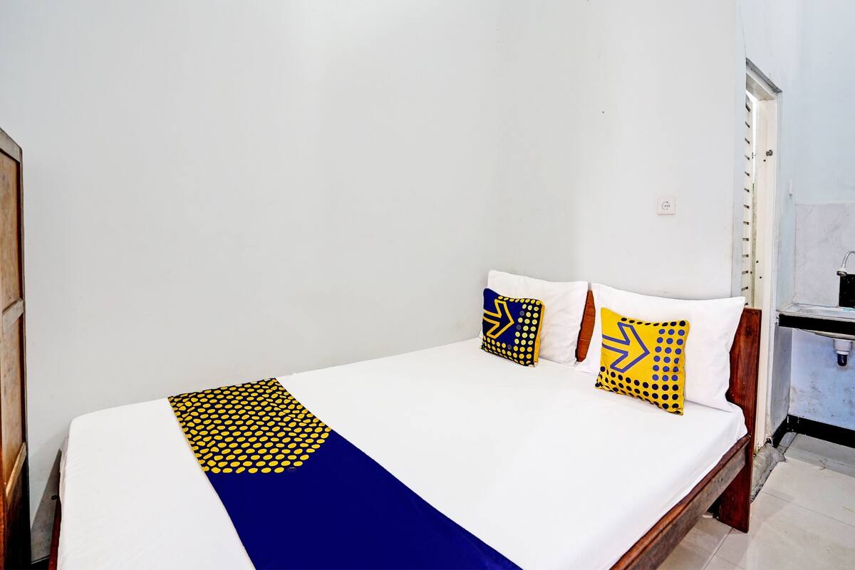 Un lit simple avec un matelas blanc, une couvre-lit à motifs bleus et jaunes, et deux oreillers aux motifs géométriques.