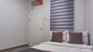 Ein Schlafzimmer mit einem Bett, weißen Wänden, einer geschlossenen Tür und einem Fenster mit horizontalen Jalousien.