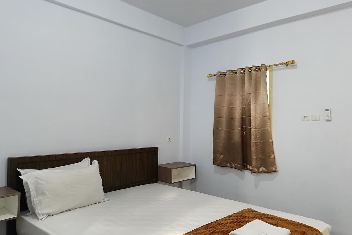 Un dormitorio con una cama, una mesita de noche, un estante en la pared y una cortina.