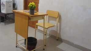 Un escritorio de madera con una silla, un cubo de basura y una planta en maceta.