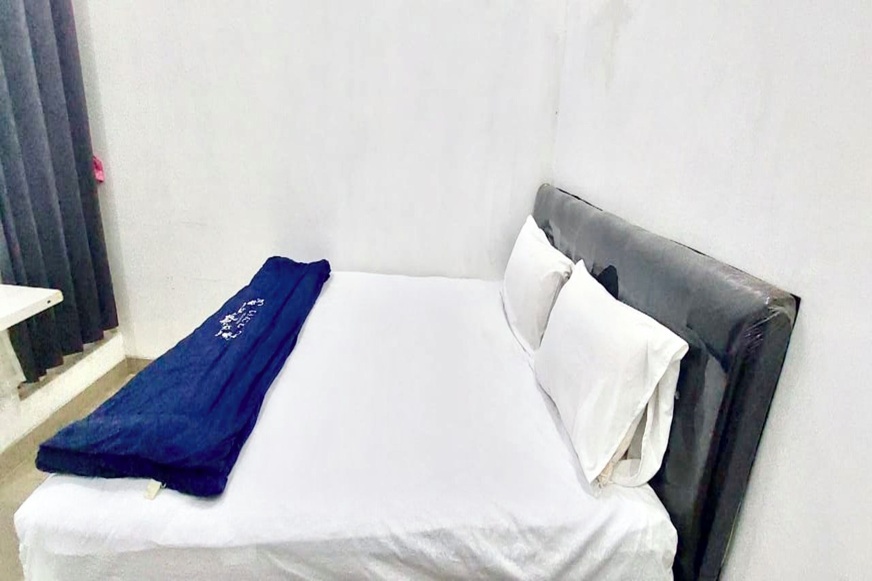 A single bed with a white mattress and a dark headboard, accompanied by a blue blanket and white pillows.