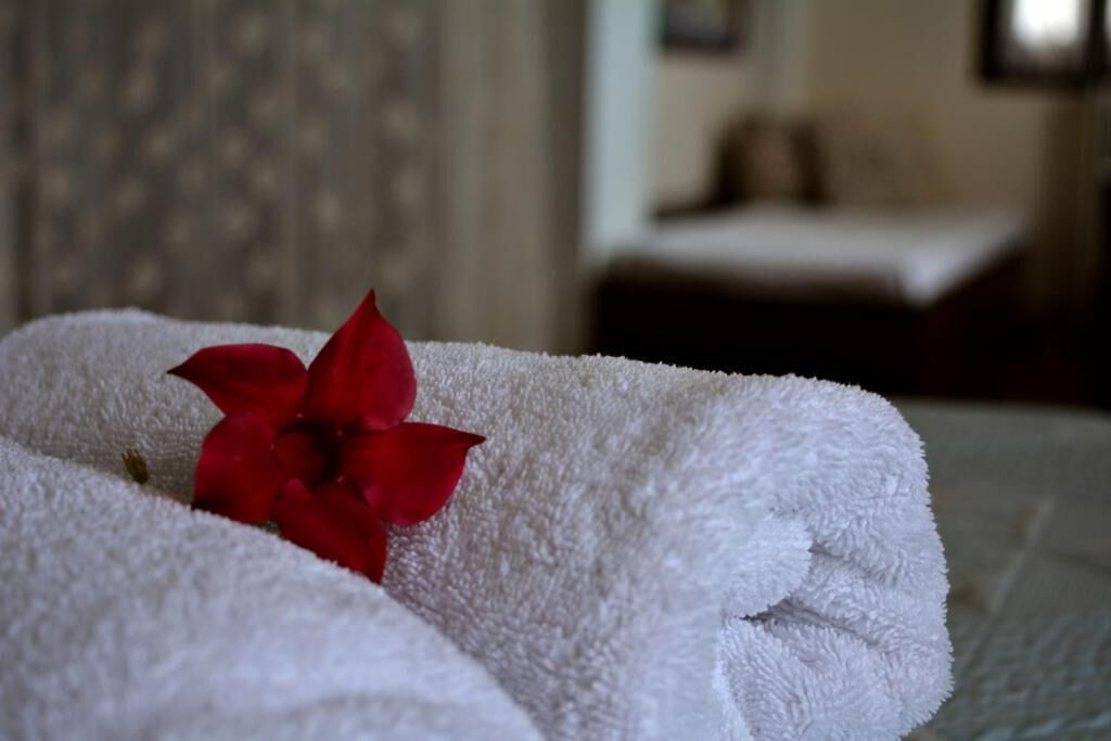 A white towel with a red flower on it, placed on a bed in a room with a blurred background.