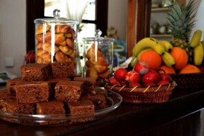 A buffet table with brownies, a fruit basket, and jars of pastries. - Guesthouse Filokalia (Volos)