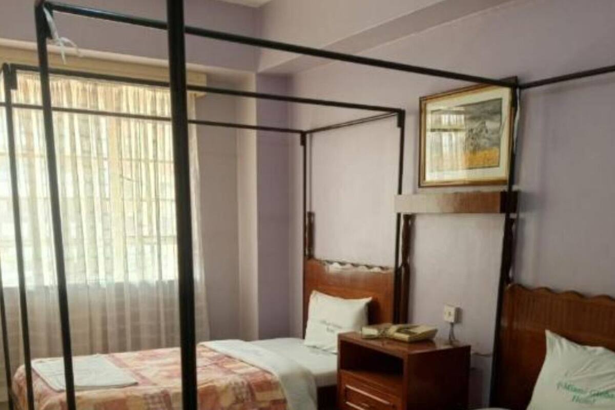 A hotel room with a four-poster bed, two single beds, a wooden nightstand, and a framed picture on the wall.