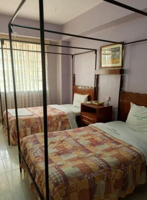 Une chambre d’hôtel avec un lit à baldaquin, deux lits simples, une table de chevet en bois et un tableau encadré au mur.