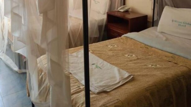 A four-poster canopy bed with a patterned bedspread, a bedside table with a lamp, and a nightstand with a phone.