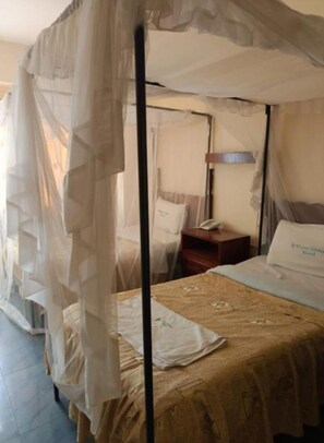 Een hemelbed met een bed met een patroon, een nachtkastje met een lamp en een nachtkastje met een telefoon.