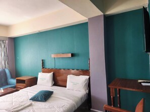 Une chambre d’hôtel comprenant un lit, une tête de lit en bois, une table de chevet et une télévision fixée au mur.