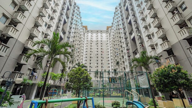 Een hoog appartementencomplex met meerdere balkons, een speeltuin en veel groen eromheen.