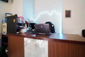 A wooden reception desk with a laptop, a water dispenser, and a neon light on the wall.