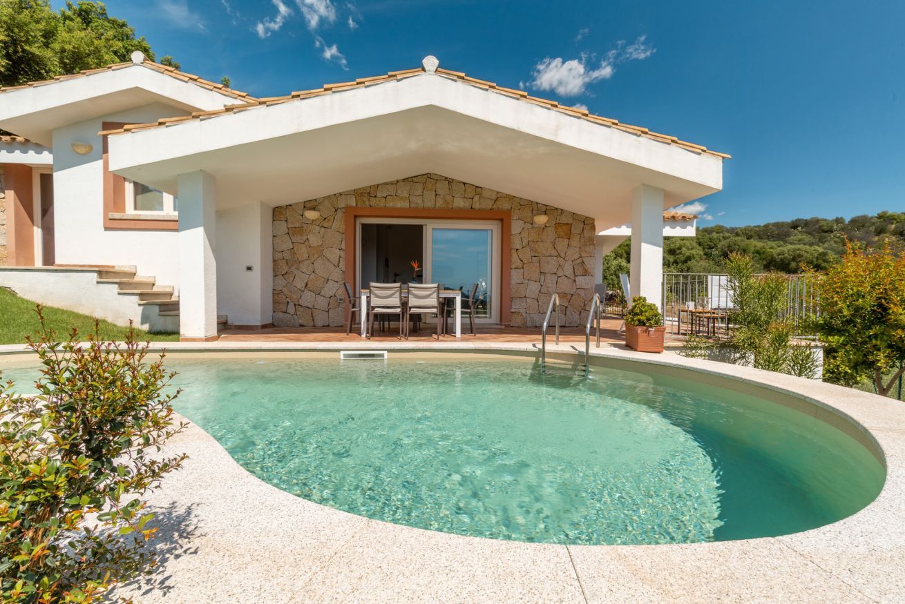 A modern house with a swimming pool, stone exterior, and a covered patio with outdoor furniture.