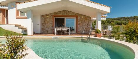 A modern house with a swimming pool, stone exterior, and a covered patio with outdoor furniture.