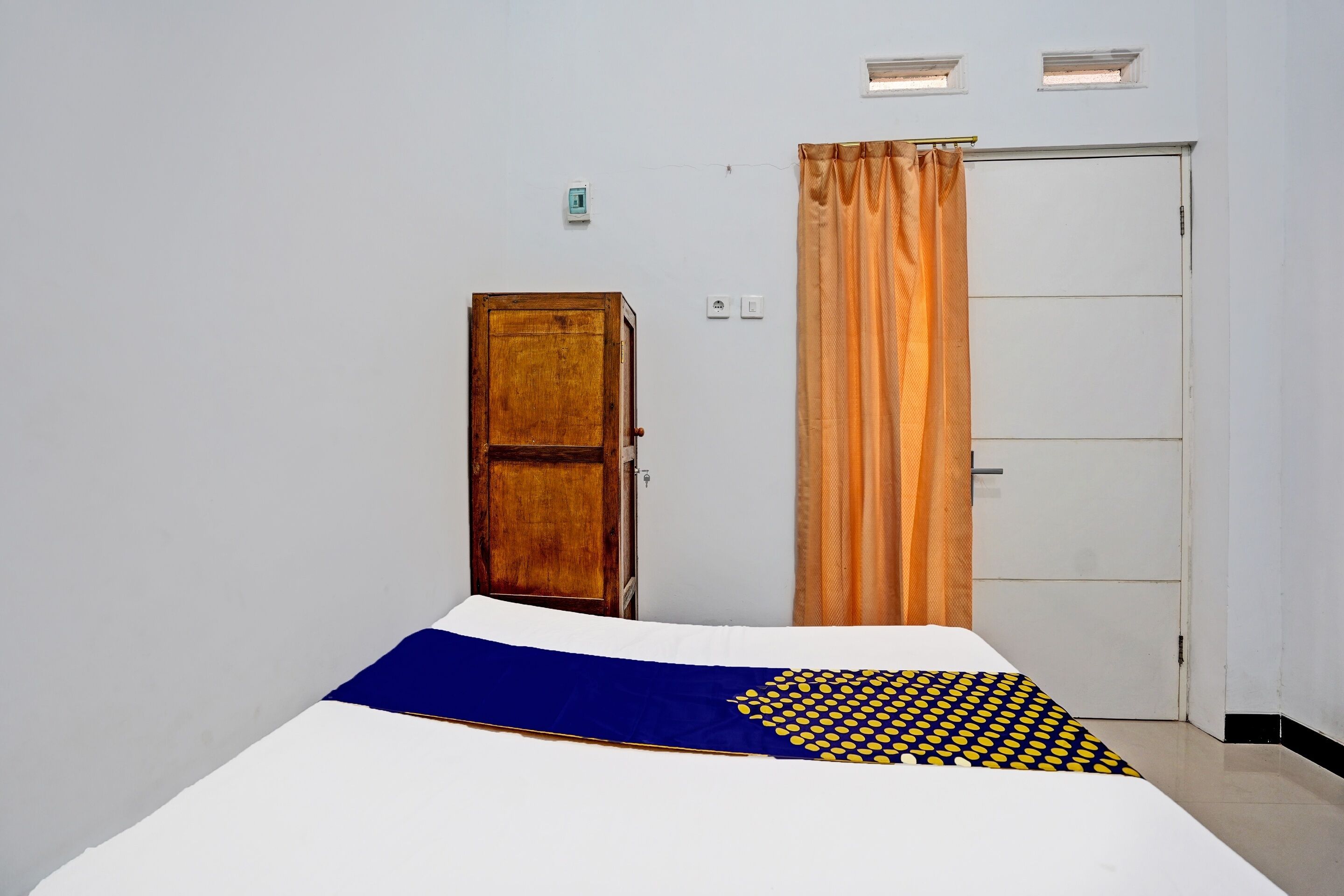 A room with a bed, a wooden door, a white wardrobe, and a curtain.