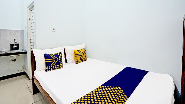 Ein Schlafzimmer mit einem Bett, zwei Kissen, einer blau-gelben Decke und einer kleinen Küchenzeile mit Spüle und Kaffeemaschine.