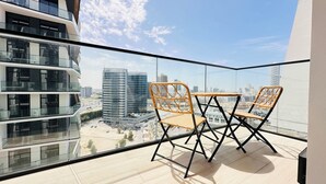 Een balkon met twee rieten stoelen en een kleine tafel, met uitzicht op een stadsgezicht met moderne gebouwen en een weg.