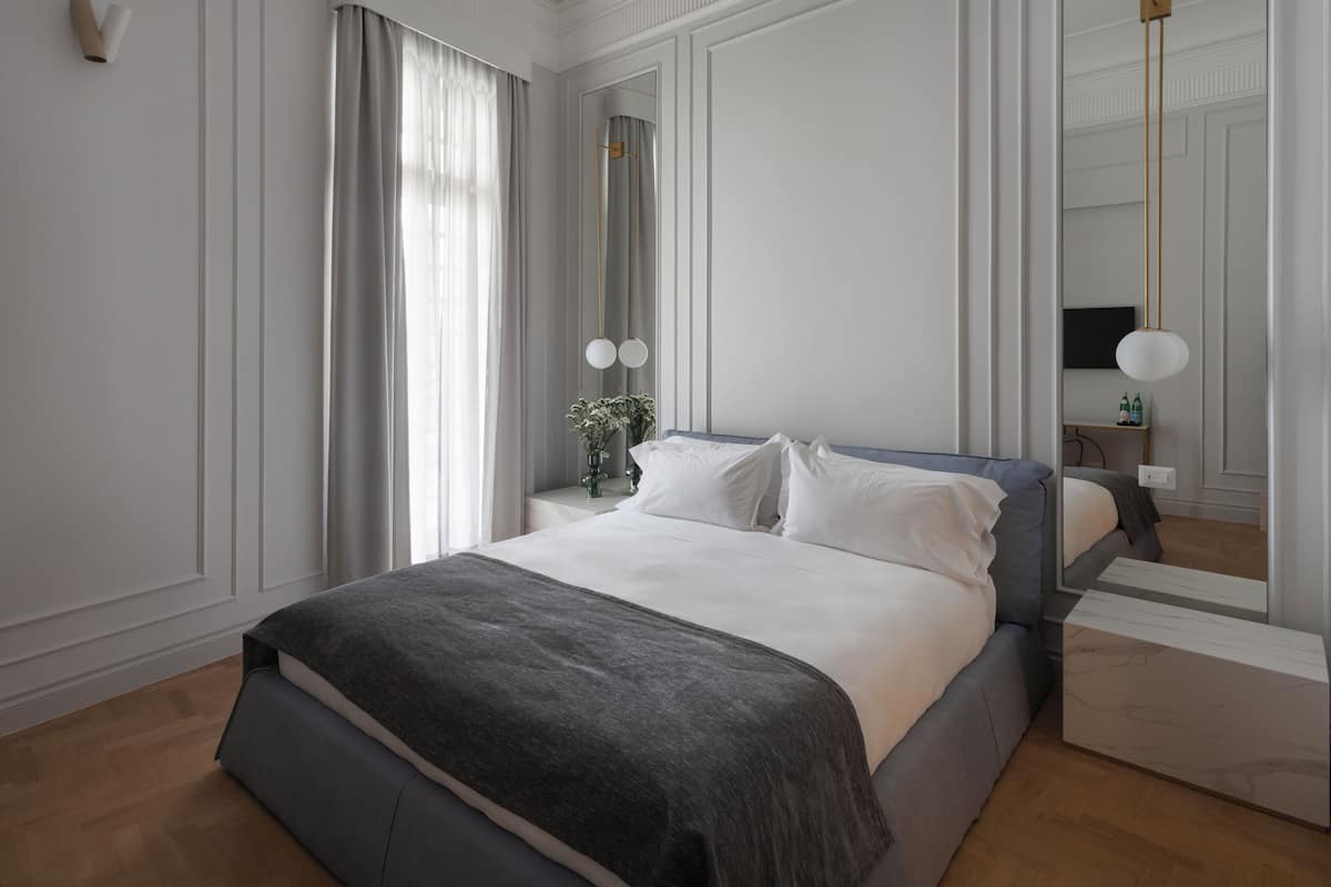 Een moderne slaapkamer met een groot bed, een nachtkastje, een spiegel en een raam met gordijnen.