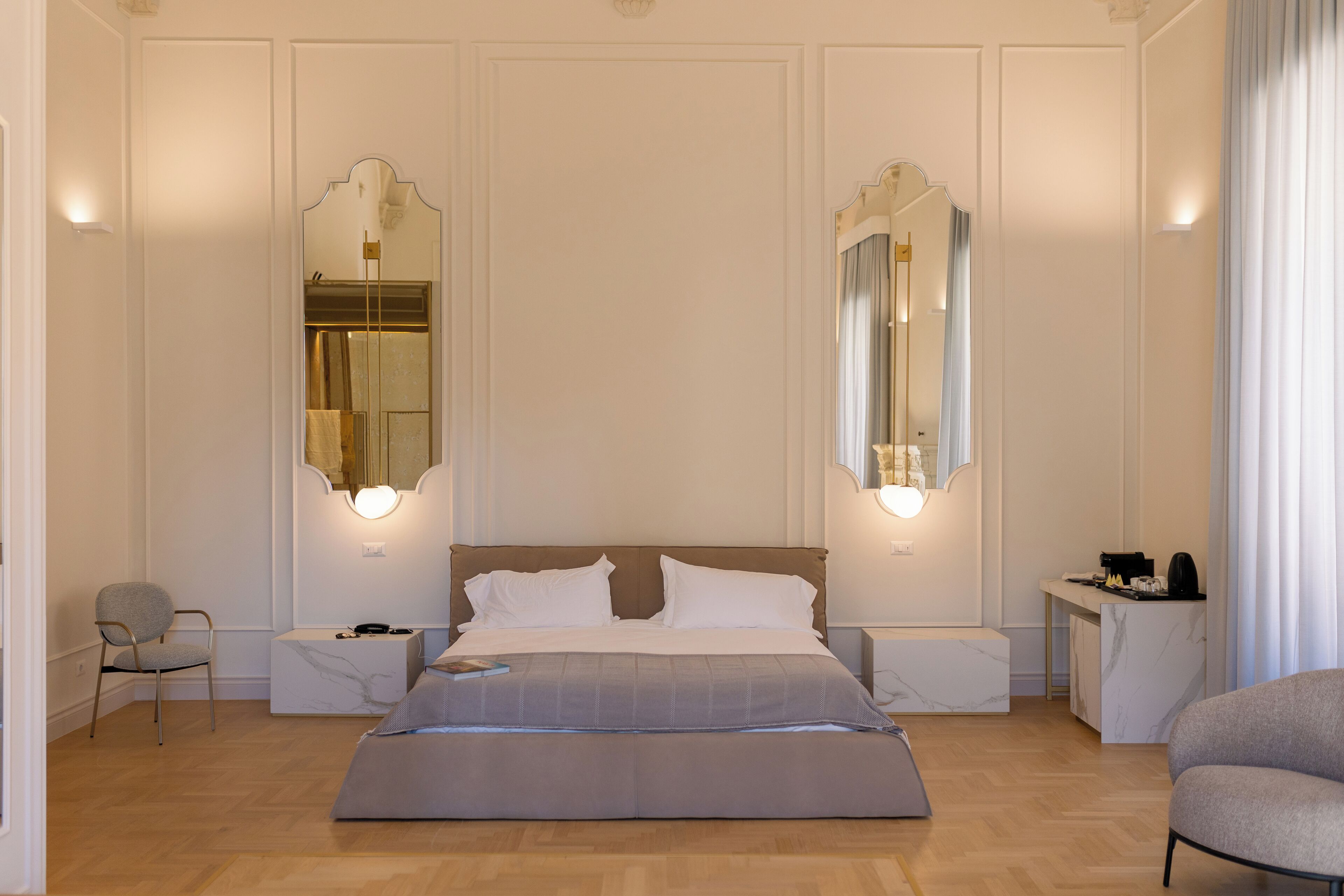 Ein Schlafzimmer mit einem großen Bett, zwei Nachttischen, einem Sessel, einem Schreibtisch und zwei Wandspiegeln.