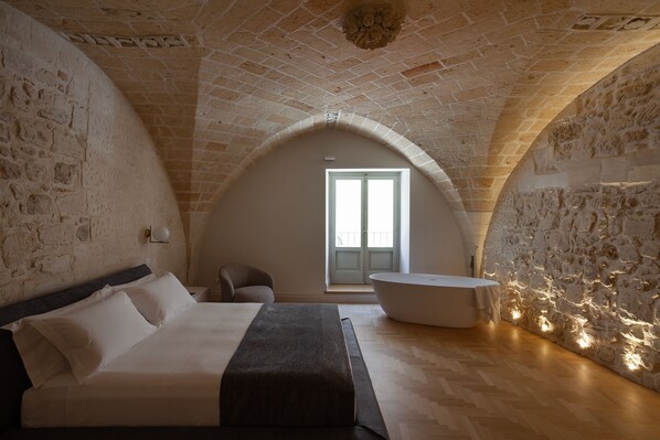 A bedroom with a large bed, a chair, a bathtub, and a view of the outside through a door.