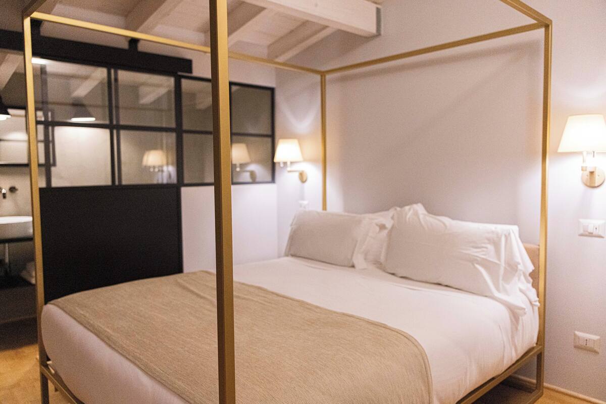 Een hemelbed met witte lakens, een houten frame en twee wandlampen.