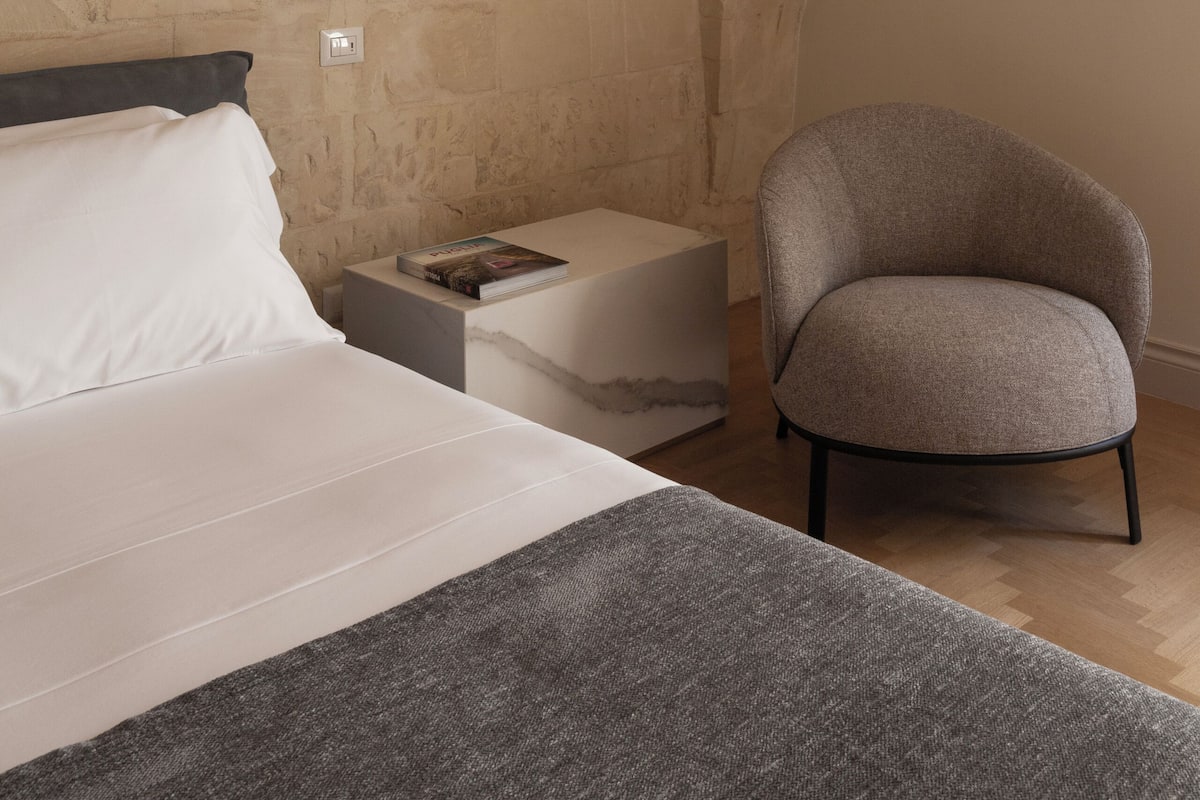 Een slaapkamer met een bed, nachtkastje, leeslamp en een stoel.