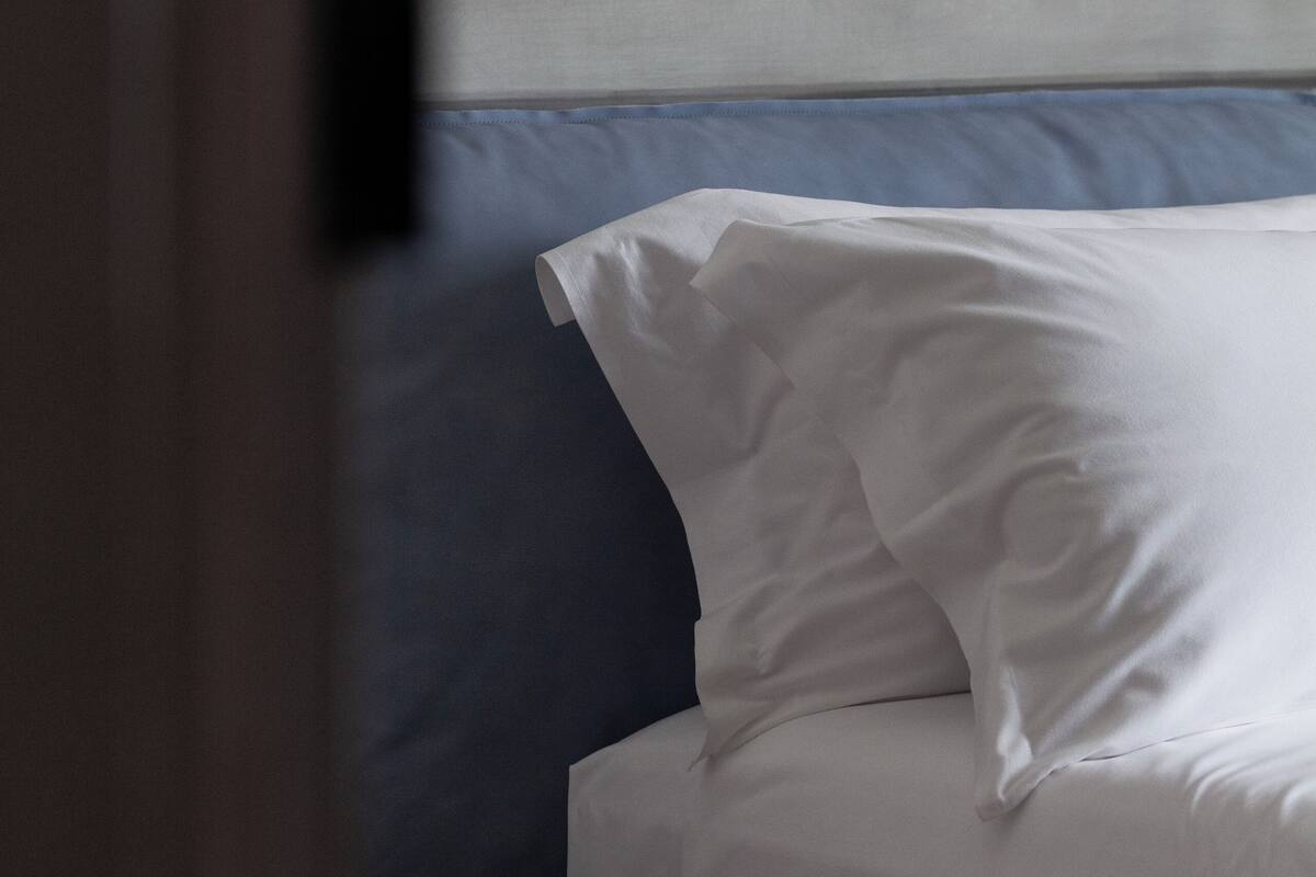 Een bed met witte lakens en een donkerblauwe hoofdbord in een kamer met een effen muur.