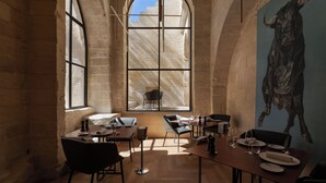 A dining area with tables and chairs, a large arched window, and a bull mural on the wall. - Palazzo Zimara Boutique Hotel - The D'Angelo Family Collection (Lecce)