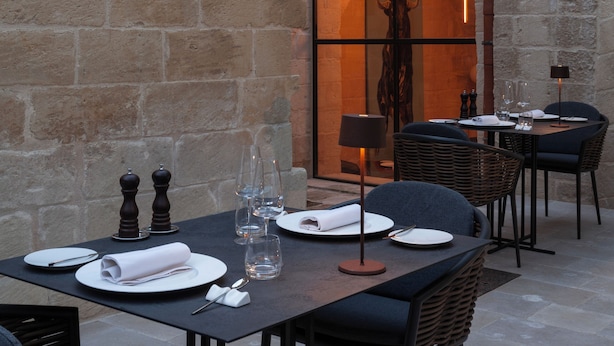 An outdoor dining area with stone walls, a large arched doorway, and wicker furniture. - Palazzo Zimara Boutique Hotel - The D'Angelo Family Collection (Lecce)