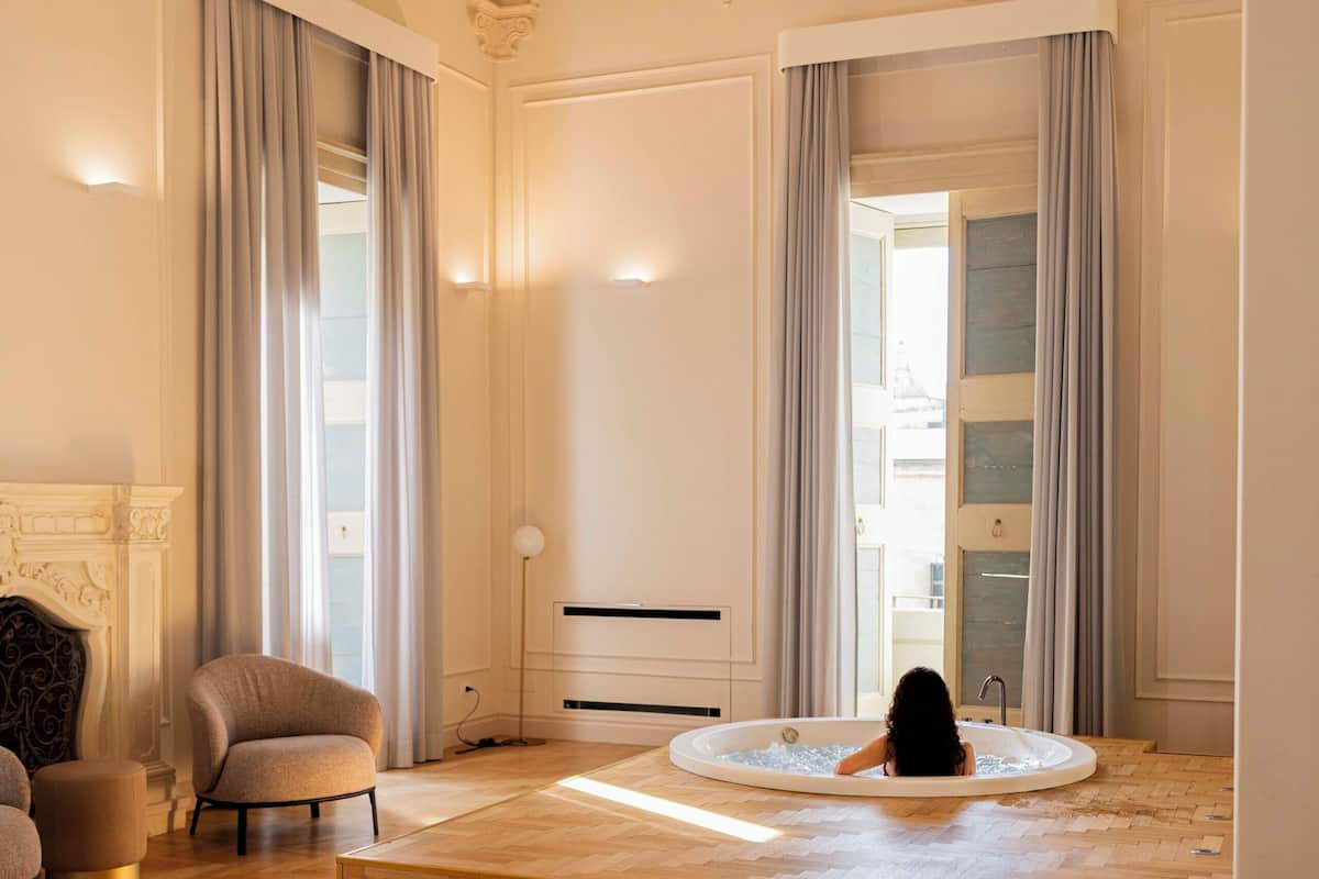 Een ruime slaapkamer met een groot bed, een zithoek met een fauteuil, een badkuip en een open haard.