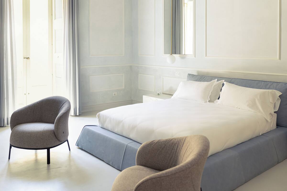 Een slaapkamer met een groot bed, twee fauteuils, een nachtkastje en een spiegel.