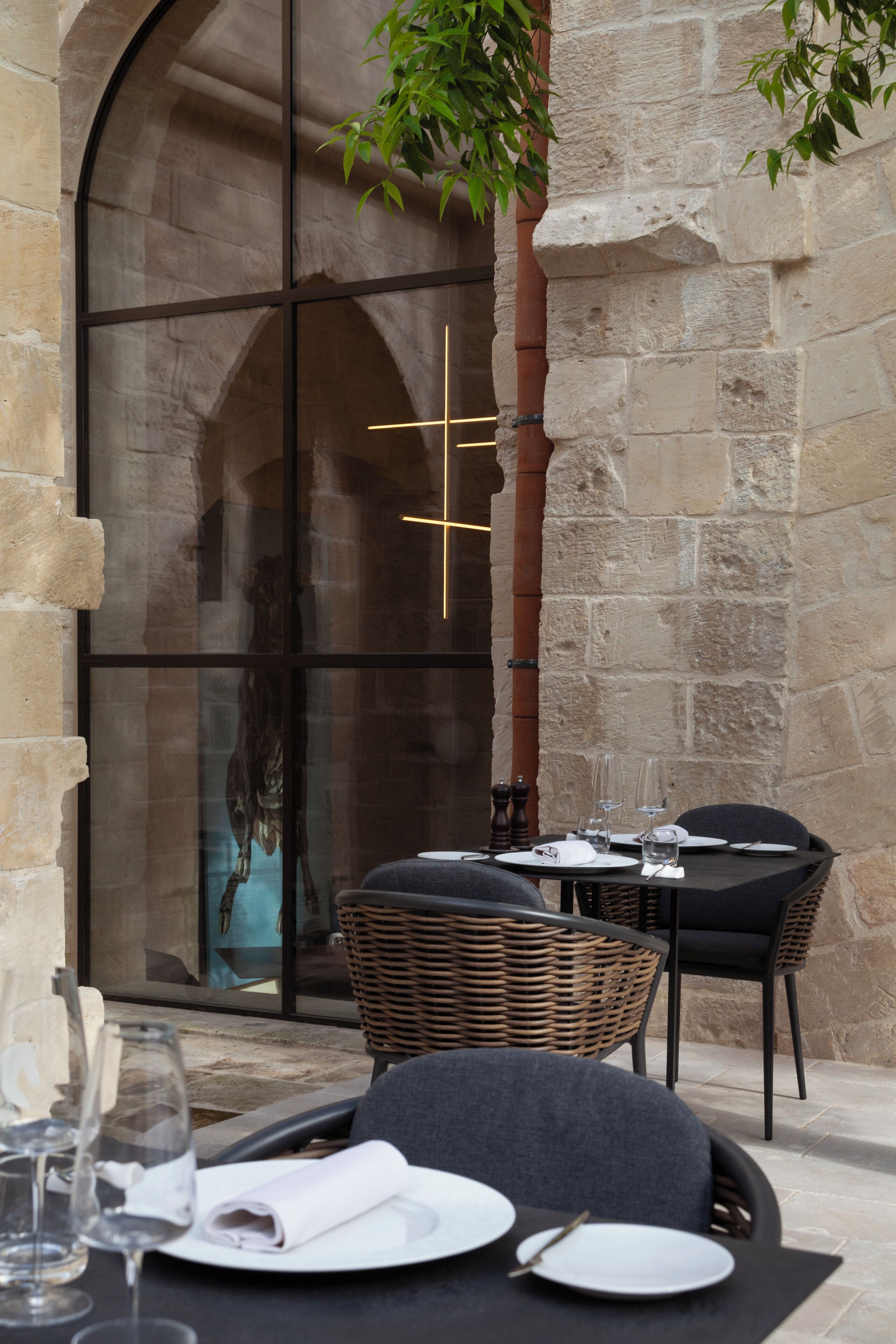 An outdoor dining area with stone walls, wicker chairs, and tables set for two.