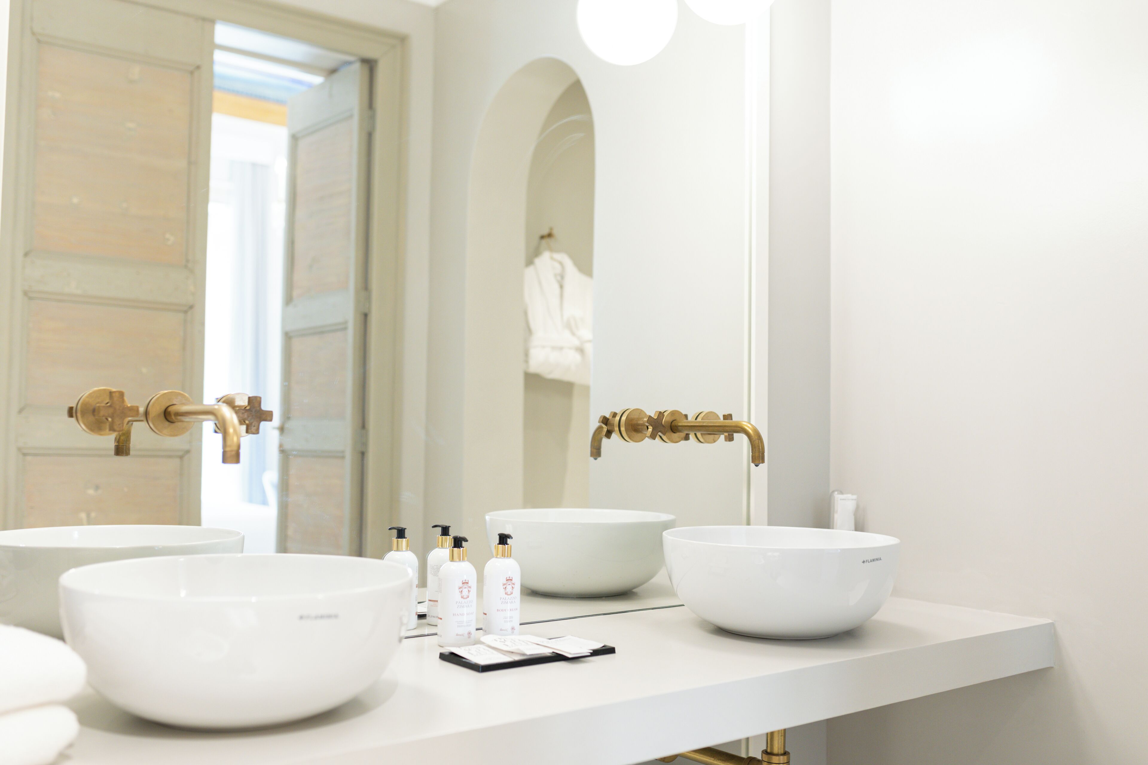 Un baño con dos lavamanos blancos tipo recipiente, grifos dorados y un espejo grande.