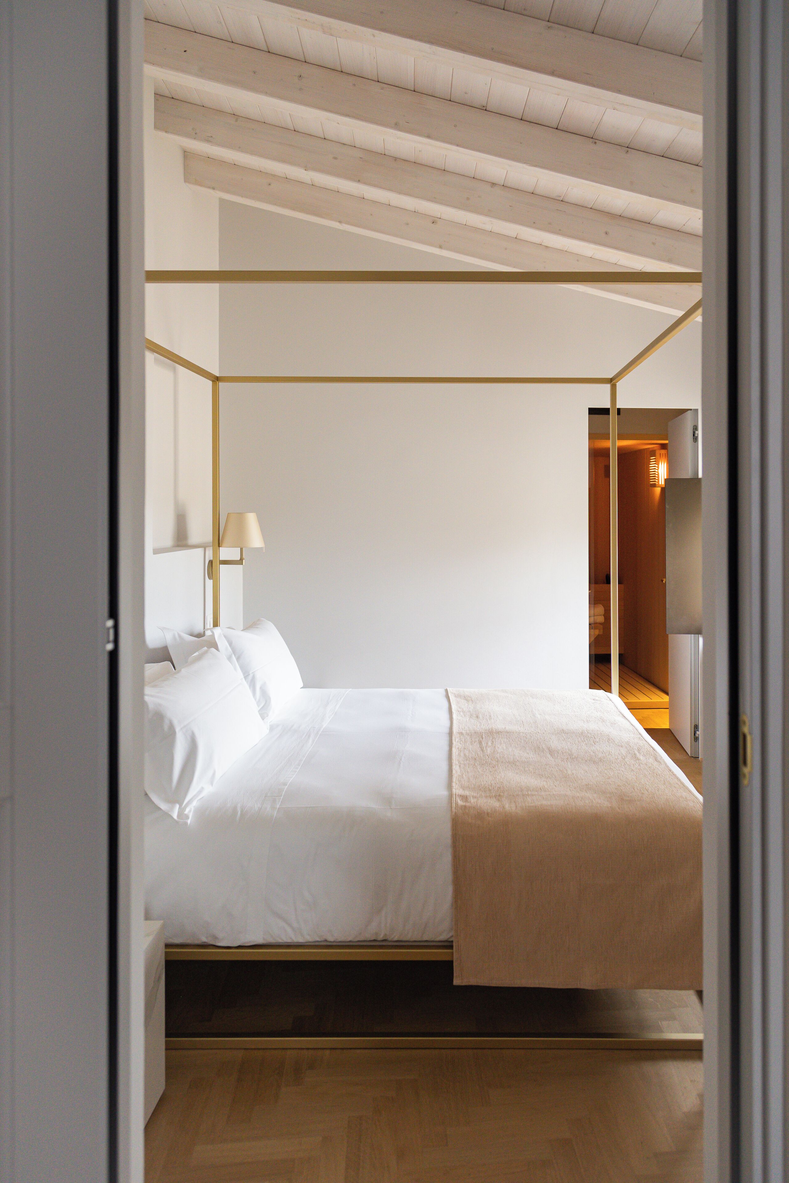 A modern bedroom with a four-poster bed, a bedside lamp, and a wooden floor.