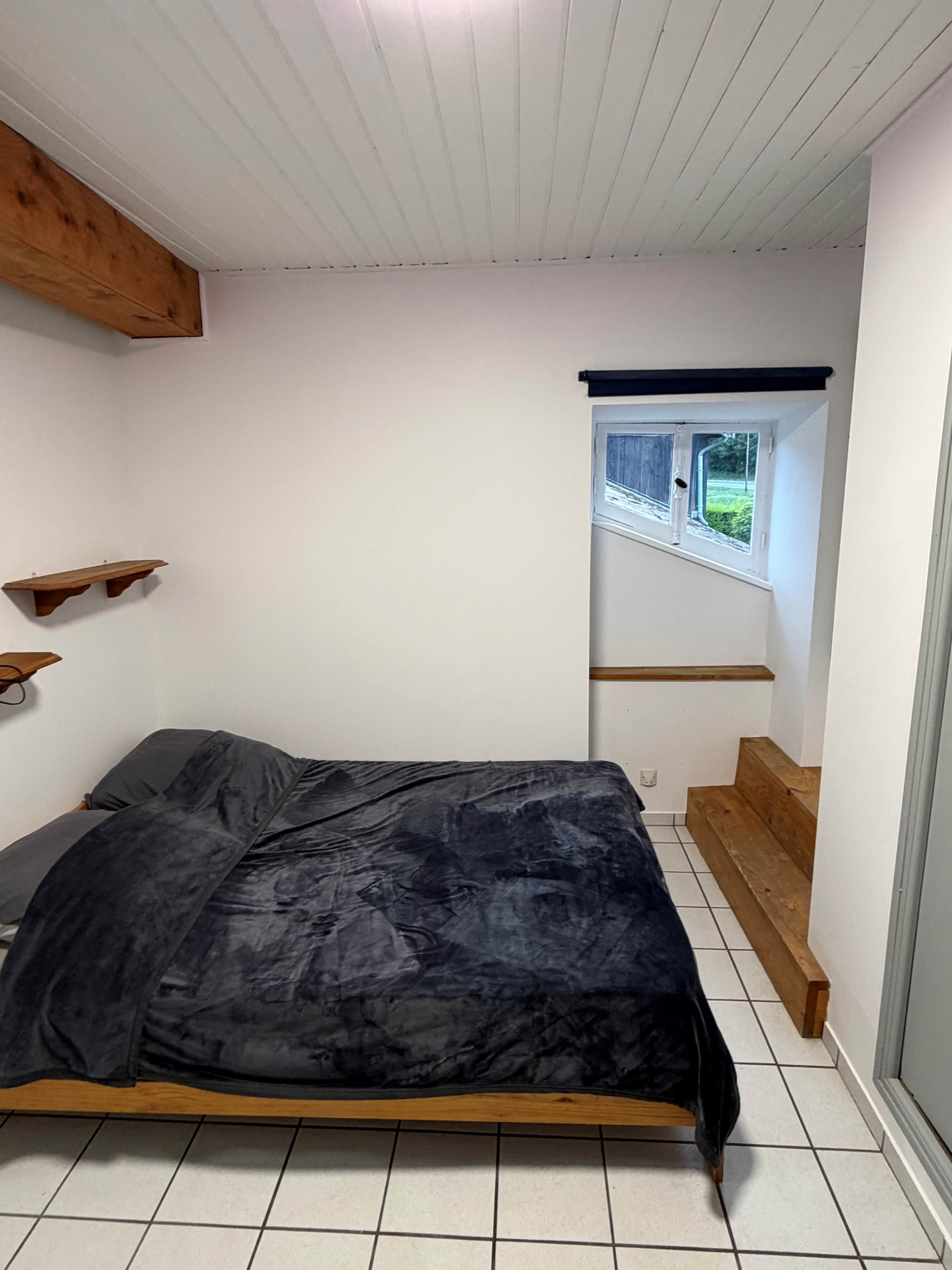 Una camera da letto con un letto, travi in legno, una finestra e vista su un paesaggio verde.