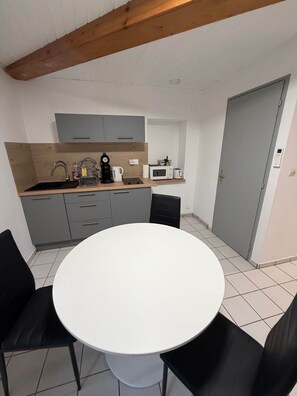 Une cuisine compacte avec des meubles gris, un plan de travail blanc et une table de salle à manger ronde, assortie de chaises noires.