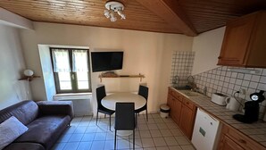 A compact kitchen with a dining table, a sofa, and a TV mounted on the wall. - Aurore - Appartement 3 Personnes (Saint-Martin-d'Uriage)